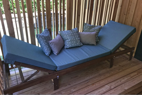 Buitenlounge met blauwe kussens op houten frame en decoratieve kussens, geplaatst op een houten terras.