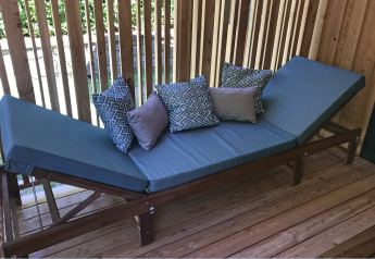 Buitenlounge met blauwe kussens op houten frame en decoratieve kussens, geplaatst op een houten terras.