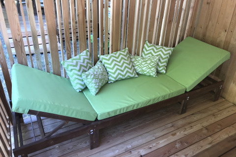 Tumbona verde con cojines estampados en SunLodge BigLeaf, situada sobre una tarima de madera y paneles.