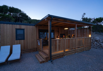 Avondbeeld van SunLodge BigLeaf, mensen op de veranda en twee ligstoelen voor de houten lodge in de natuur.