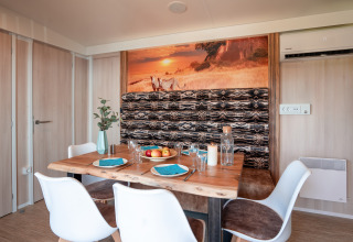 Comedor en SunLodge BigLeaf con mesa de madera, sillas blancas y decoración de pared africana al atardecer.