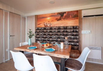 Eethoek in SunLodge BigLeaf met houten tafel, witte stoelen en Afrikaanse wanddecoratie.