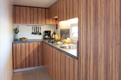 Modern SunLodge BigLeaf kitchen with wood cabinetry, stove, sink, coffee maker, and cooking utensils.
