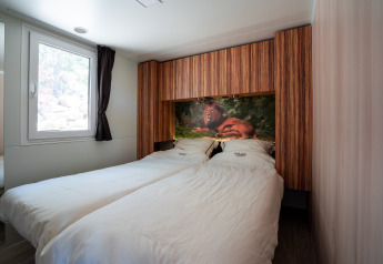 Slaapkamer in SunLodge BigLeaf met twee aparte bedden, houtpanelen en een leeuwenafbeelding boven het bed.