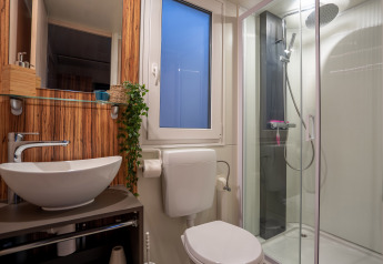 Baño moderno en SunLodge BigLeaf con ducha acristalada, inodoro, lavabo y pared de madera.