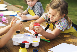 Bambini che fanno attività artistiche all’aperto in una sistemazione glamping con colori e carta.