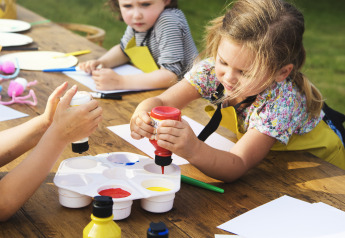 Niños haciendo manualidades al aire libre en un alojamiento glamping usando pinturas y papel.