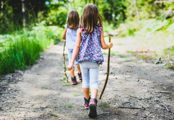 Due bambini camminano su un sentiero nel bosco con bastoni durante un soggiorno glamping nella natura.