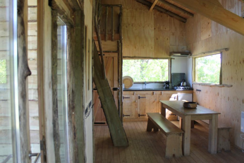 Innenansicht des Baumhauses bei Beloofde Land, Niederlande, mit Holzmöbeln und großem Fenster.
