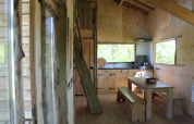 Innenansicht des Baumhauses bei Beloofde Land, Niederlande, mit Holzmöbeln und großem Fenster.