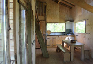 Vue intérieure de la cabane dans les arbres à Beloofde Land, Pays-Bas, avec cuisine et bancs en bois.