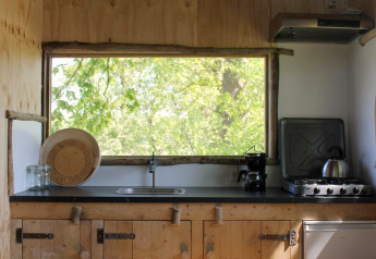 Rustic treehouse kitchen with large window overlooking green trees at Treehouse at Beloofde Land, Netherlands.