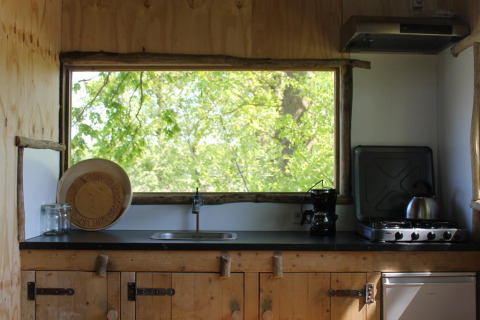 Rustic treehouse kitchen with large window overlooking green trees at Treehouse at Beloofde Land, Netherlands.