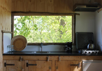 Træhuskøkken med stort vindue og udsigt over grønne træer i Treehouse at Beloofde Land, Holland.