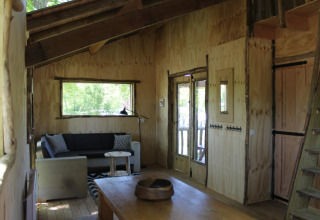 Interno accogliente di una casa sull'albero al Beloofde Land, Paesi Bassi, con pareti in legno e divano.