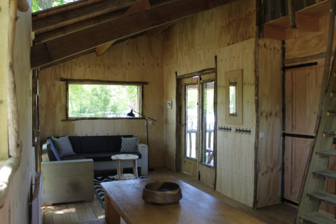 Gemütliches Baumhaus-Interieur im Beloofde Land, Niederlande, mit Holzwänden und Sofa am Fenster.