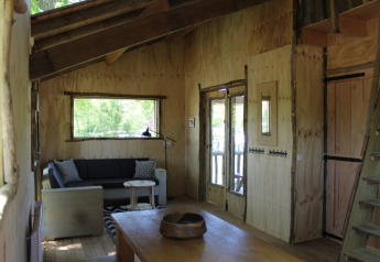 Interior acogedor de casa del árbol en Beloofde Land, Países Bajos, con paredes de madera y sofá sencillo.