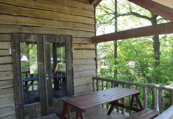 Terrasse de cabane dans les arbres avec table en bois, entourée de verdure, Beloofde Land, Pays-Bas.