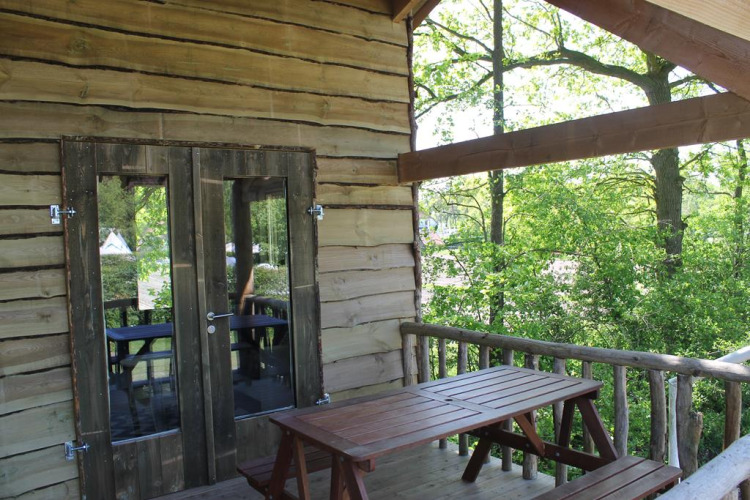 Baumhaus Terrasse mit Holztisch und Bänken, umgeben von grünen Bäumen, Beloofde Land, Niederlande.