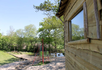 Treehouse at Beloofde Land in the Netherlands, surrounded by trees, with a playground and bench nearby.