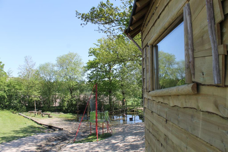 Baumhaus am Beloofde Land in den Niederlanden, von Bäumen umgeben, mit Spielplatz und Bank.