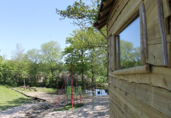 Casa del árbol en Beloofde Land, Países Bajos, rodeada de árboles, con parque infantil y bancos.