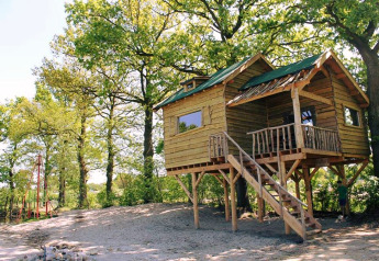 Treehouse with porch and stairs among trees at Beloofde Land, Netherlands, on a sunny day.