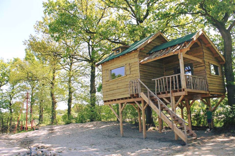 Baumhaus mit Veranda und Treppe im Wald, Beloofde Land, Niederlande, an einem sonnigen Tag.