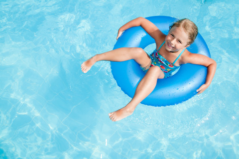 Niña relajándose en un flotador azul dentro de la piscina en un alojamiento de glamping soleado.