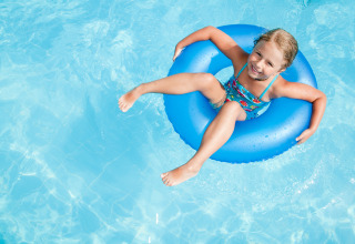Niña relajándose en un flotador azul dentro de la piscina en un alojamiento de glamping soleado.