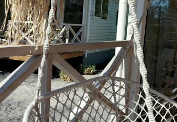 Silla hamaca blanca en un porche de madera en Beach House, Beloofde Land, Países Bajos, con cielo azul.