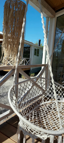 Hvid hængekøjestol på en træveranda ved Beach House, Beloofde Land, med solskin og blå himmel.