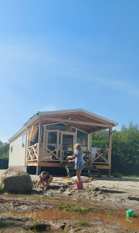 Due bambini giocano nel fango davanti a una casa sulla spiaggia a Beloofde Land, Paesi Bassi, cielo sereno.