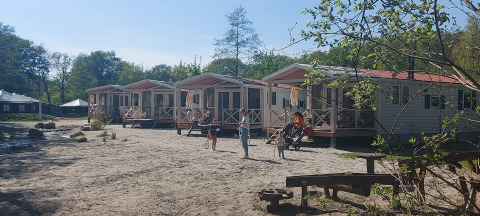 Fila de casas de playa en Beloofde Land, Países Bajos, con familias en porches y niños jugando fuera.