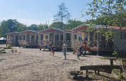 Fila de casas de playa en Beloofde Land, Países Bajos, con familias en porches y niños jugando fuera.