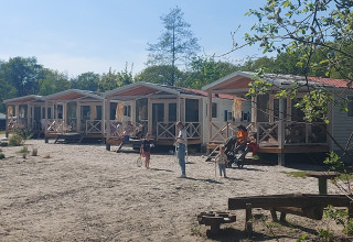 Fila de casas de playa en Beloofde Land, Países Bajos, con familias en porches y niños jugando fuera.