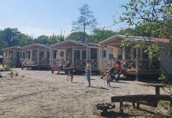 Fila de casas de playa en Beloofde Land, Países Bajos, con familias en porches y niños jugando fuera.