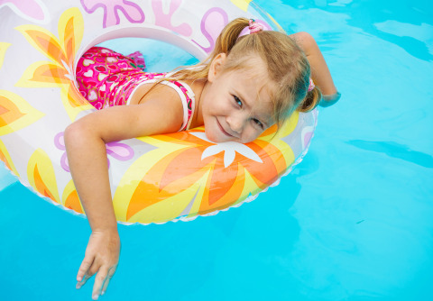 Kleines Mädchen mit pinkem Badeanzug und Schwimmreifen entspannt am Pool im Beach House, Niederlande.