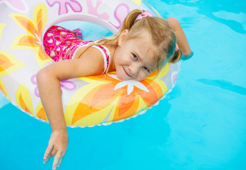 Kleines Mädchen mit pinkem Badeanzug und Schwimmreifen entspannt am Pool im Beach House, Niederlande.