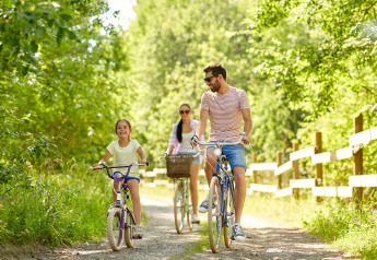 Familie fährt gemeinsam Fahrrad auf einem Waldweg neben einem Zaun bei einem Glamping-Abenteuer.
