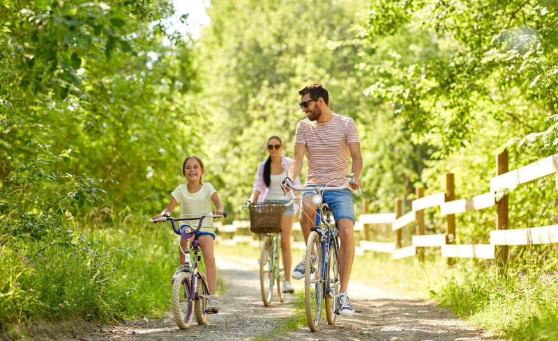 Famiglia in bicicletta su un sentiero immerso nel verde durante una vacanza glamping nella natura.