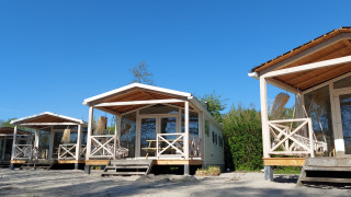 Tre strandhuse af træ ved naturhuset Beach House med veranda under en klar blå himmel om dagen.
