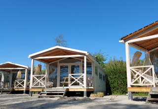 Drie houten strandhuisjes bij Nature house Beach House met veranda’s onder een blauwe hemel.