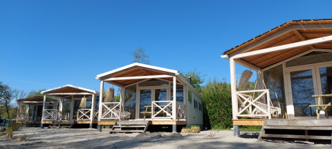 Drie houten strandhuisjes bij Nature house Beach House met veranda’s onder een heldere blauwe lucht.