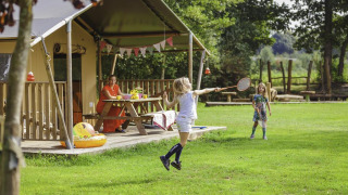 Des enfants jouent au badminton devant une tente safari à Beloofde Land, Pays-Bas, sous le regard d'une femme.