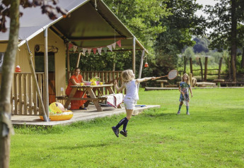 Bambini giocano a badminton davanti a una tenda safari al Beloofde Land, Paesi Bassi, con una donna vicina.