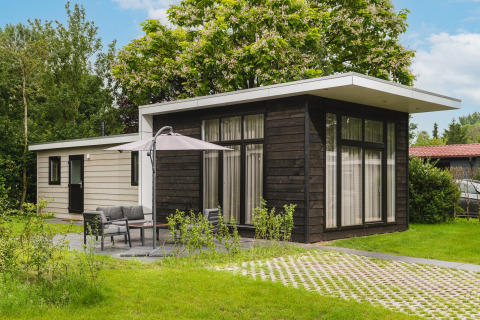 Vista exterior de la Cosy Cabin con fachada moderna blanca y negra, césped verde y muebles de jardín.