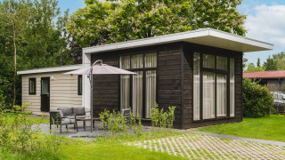 Outdoor view of Cosy Cabin with modern black and white exterior, green lawn, and patio furniture set.