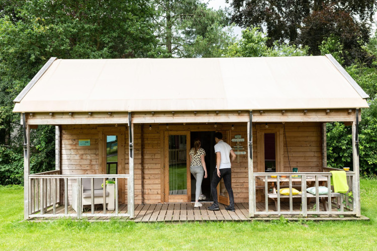 Zwei Personen betreten ein Boerderij-Safari-Zelt im Beloofde Land in den Niederlanden, umgeben von Bäumen.
