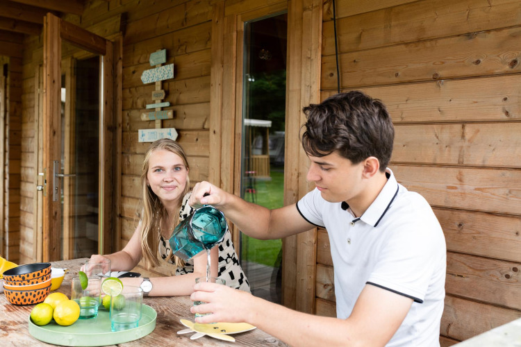 Twee jonge volwassenen genieten samen van een drankje op het houten terras bij een safaritent.